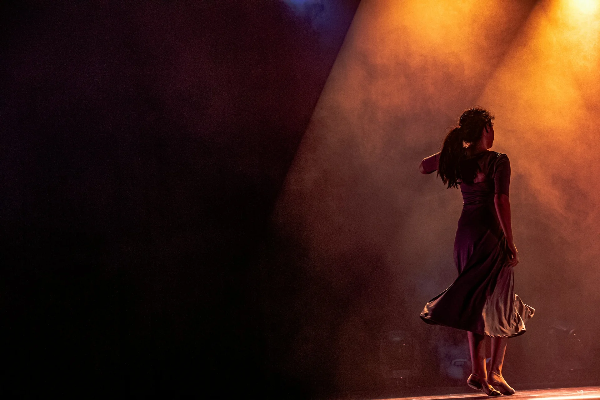 A dancer mid-turn on stage under warm spotlight and stage smoke